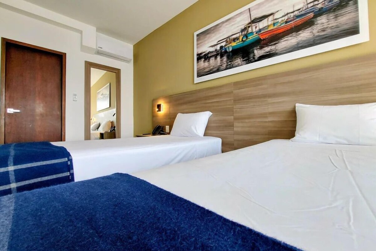 A hotel room with two beds, a wooden headboard, a painting of boats, and a mirror.