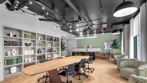 Un espace de bureau moderne avec une longue table de conférence en bois, des chaises de bureau noires et une bibliothèque remplie de livres et d’objets décoratifs.