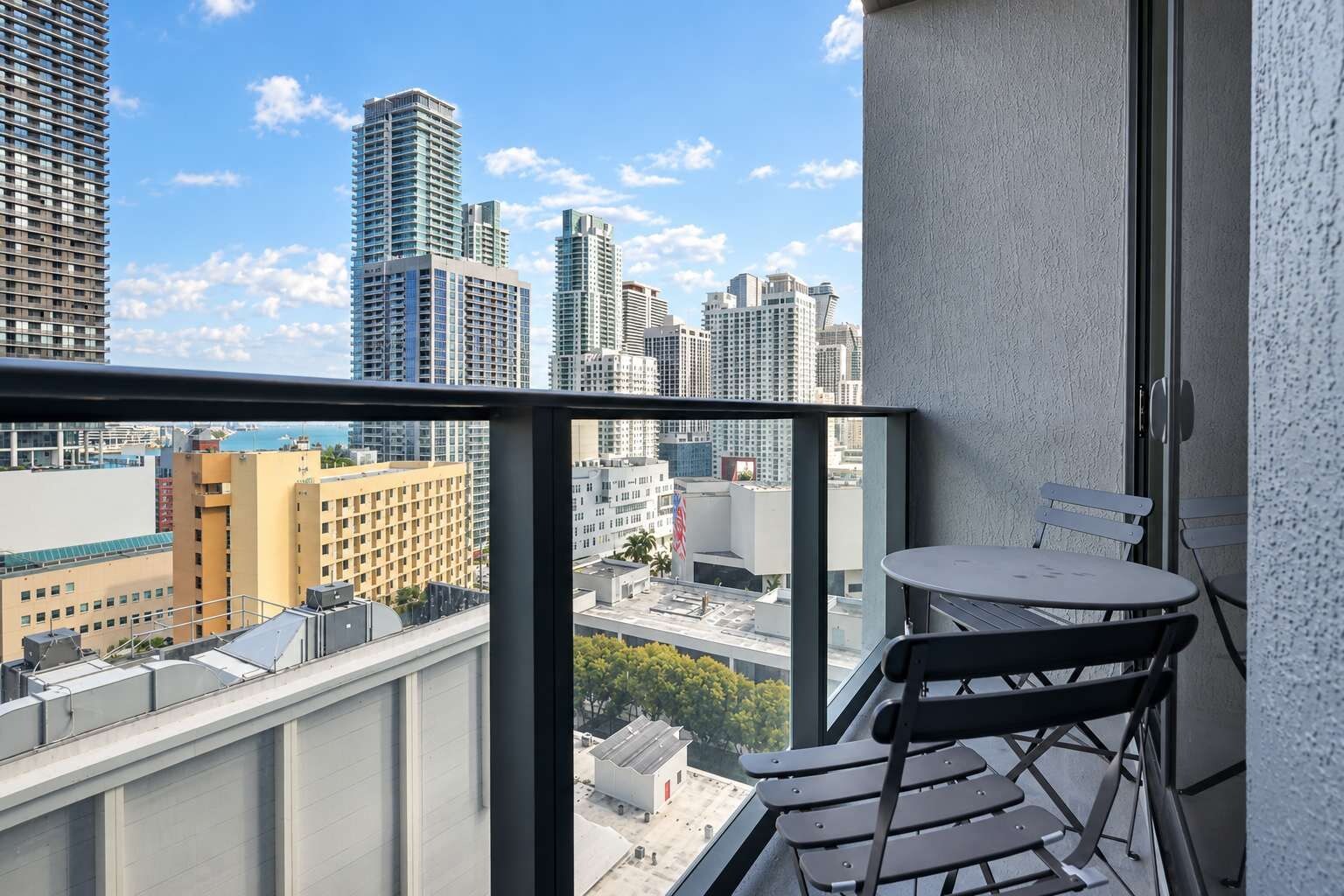 A balcony with a table and chairs, overlooking a cityscape with high-rise buildings.