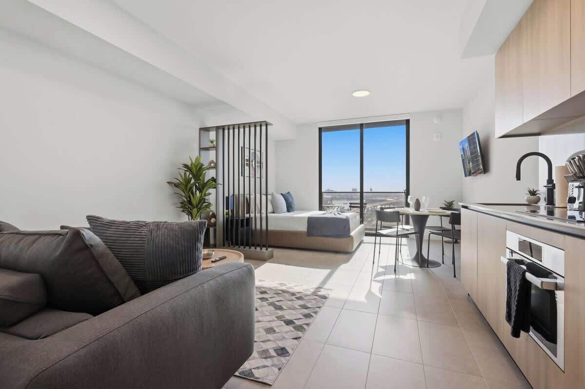 Eine moderne Wohnung mit Wohnbereich, Küchenzeile und einem Balkon mit Blick auf die Stadt.