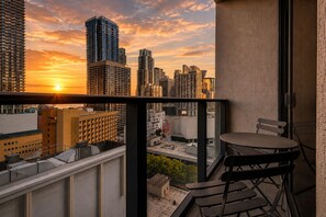A balcony with a table and chairs, overlooking a cityscape with high-rise buildings during sunset. - Elegant 1 Bedroom | Premium Resort-Style Living (Miami)