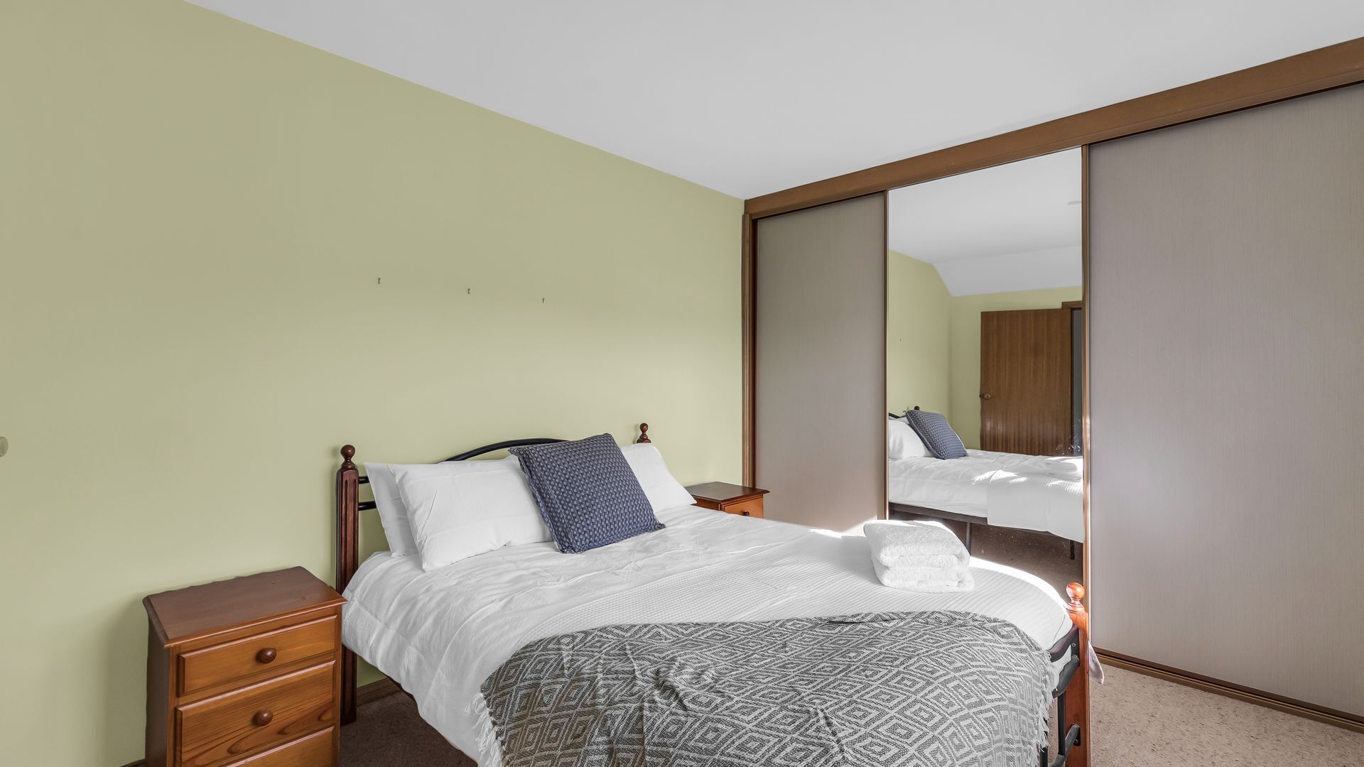 Un dormitorio con una cama, una mesita de noche de madera, un espejo y un armario.
