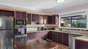 Eine kompakte Küche mit Kühlschrank, Mikrowelle, Backofen und einem Fenster mit Blick ins Grüne.