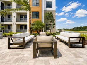 A modern outdoor seating area with a pool view, surrounded by a multi-story building with balconies. - 2BR Luxury North Retreat with Pool and Gym (Naples)