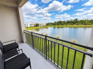 A balcony with a view of a lake, a grassy area, and a row of buildings in the background. - Luxury North Retreat with Pool and Gym (Naples)