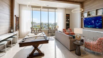 Una sala de estar moderna con mesa de billar, asientos cómodos, un televisor y un ventanal con vistas a la ciudad.