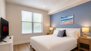 A hotel room with a bed, a TV displaying the Netflix logo, a window with blinds, a painting on the wall, and two bedside lamps. - Luxury North Retreat with Pool and Gym (Naples)