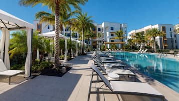 Un área de piscina en un resort con sillones de descanso, palmeras y edificios modernos.