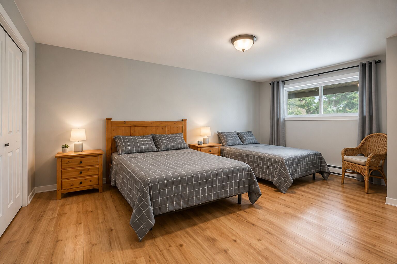 A bedroom with two beds, wooden nightstands, a wicker chair, a window with curtains, and a ceiling light.
