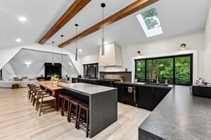 A modern kitchen with a large island, wooden bar stools, and a view of the outdoors through a large window.