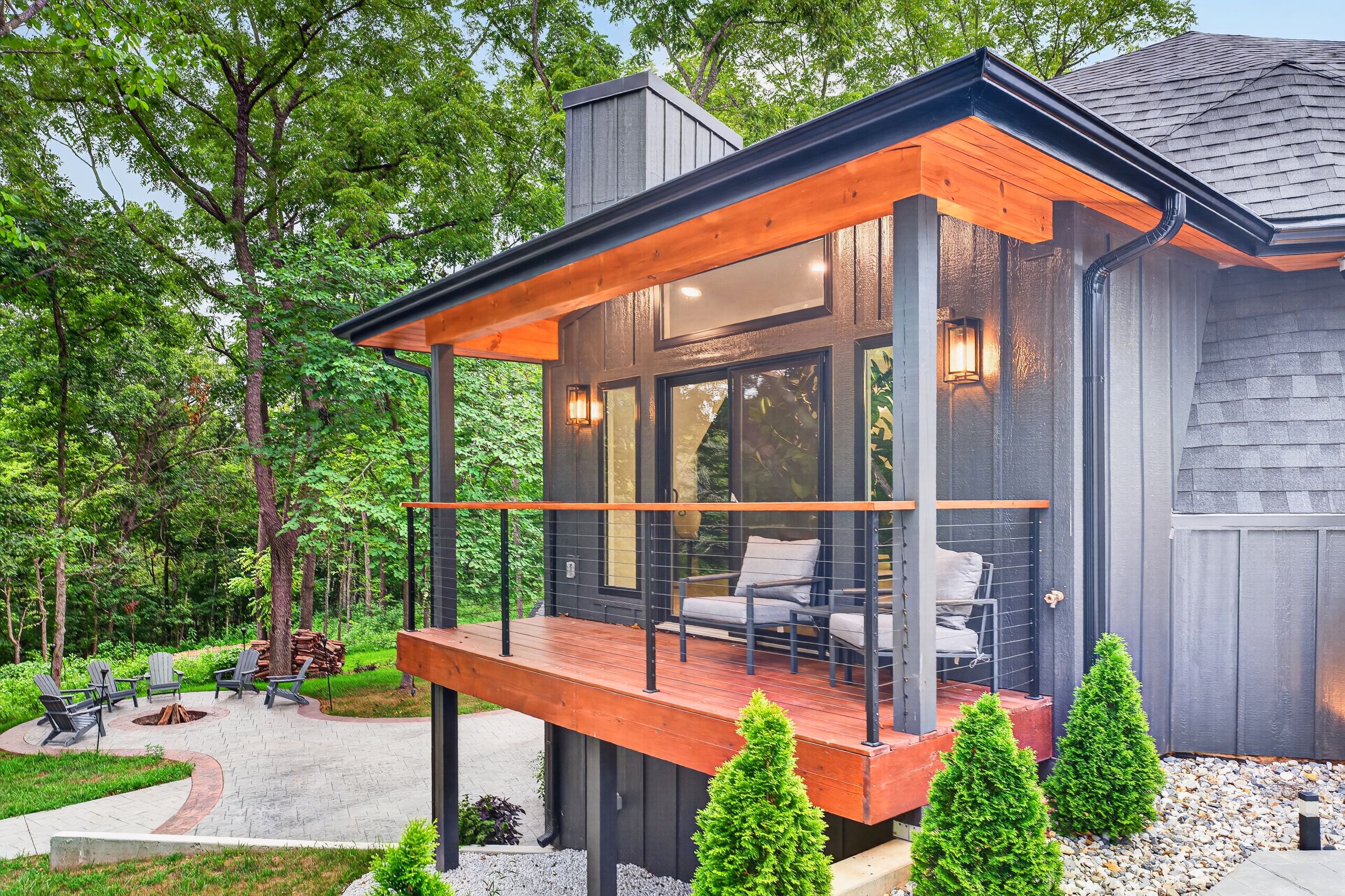 Una casa moderna con terraza de madera, mobiliario exterior y una chimenea.