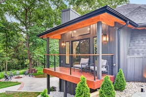 A modern house with a wooden deck, outdoor seating, and a fire pit.