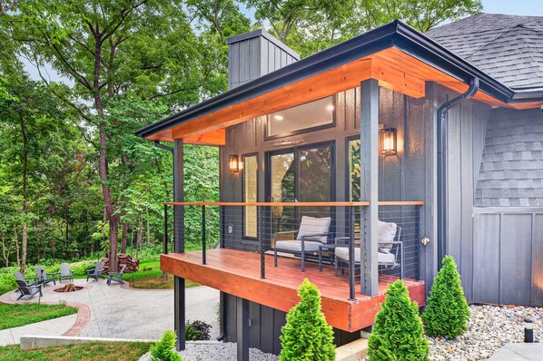 Ein modernes Haus mit einer Holzterrasse, Sitzgelegenheiten im Freien und einem Feuerkorb.