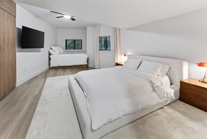 Ein modernes Schlafzimmer mit einem großen Bett, Nachttischen, einem Flachbildfernseher und einem Fenster mit Jalousien.