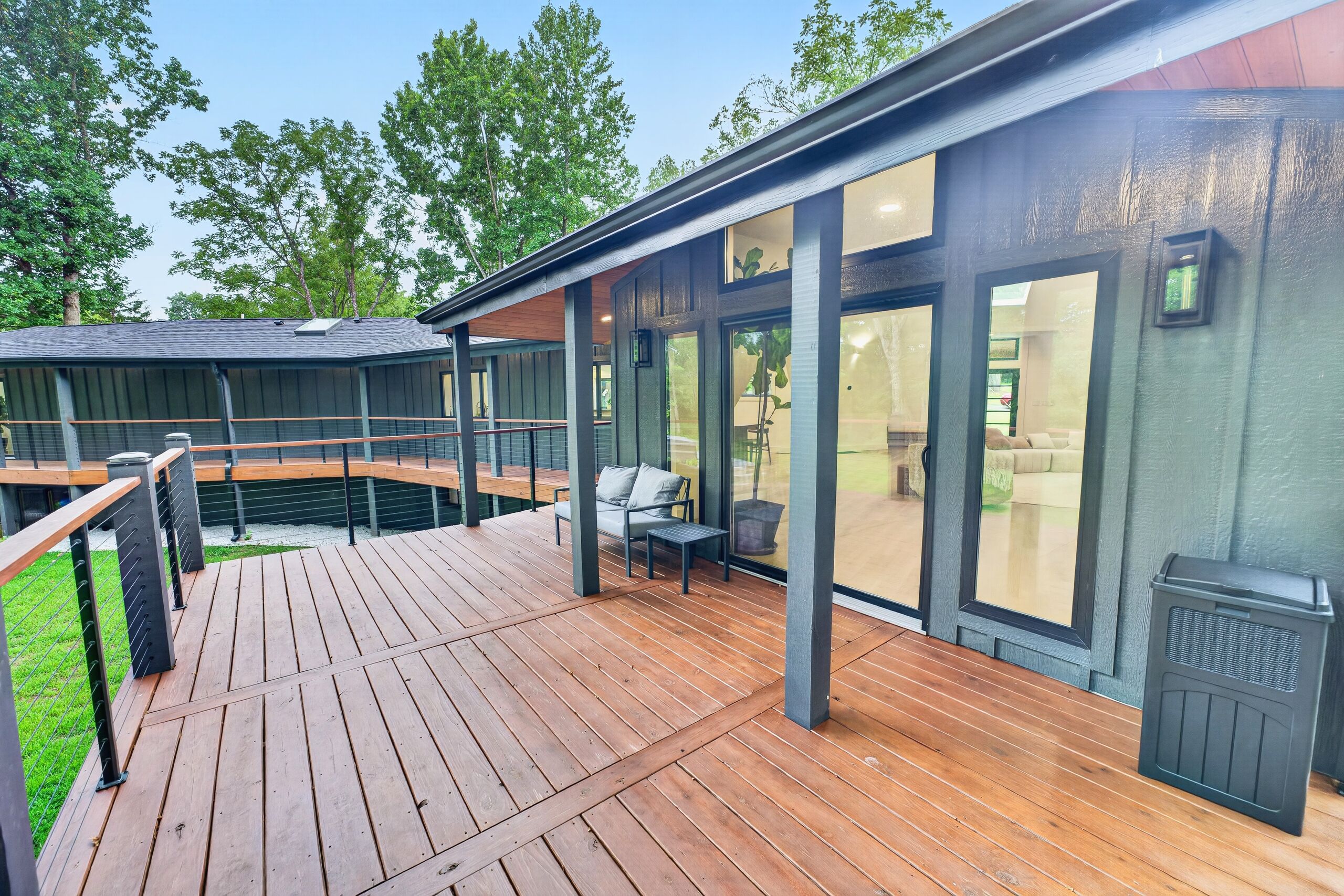 A modern outdoor deck with a wooden floor and metal railings, overlooking a landscaped area with trees.