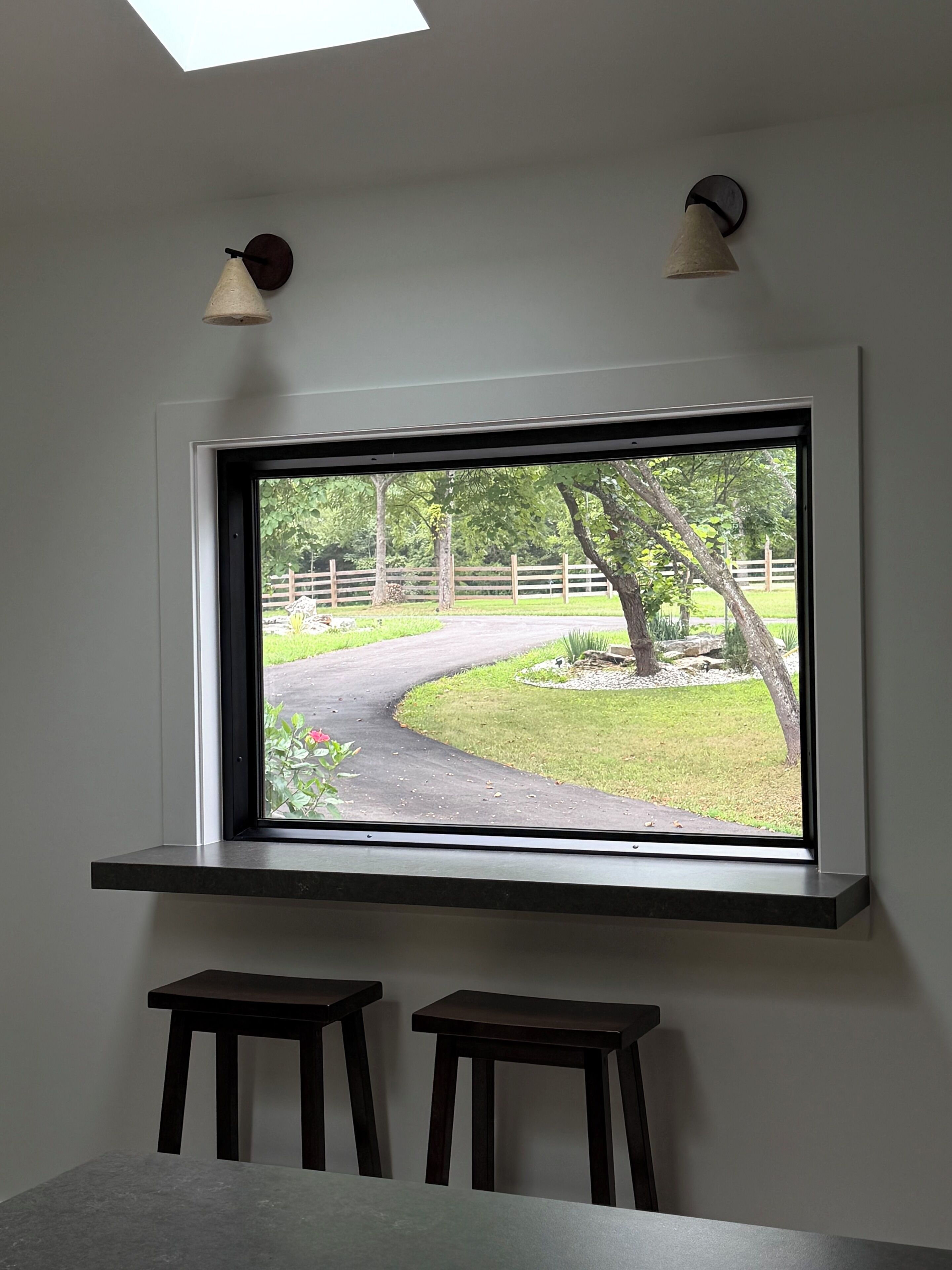 A room with a large window, two stools, and a wall-mounted light fixture.