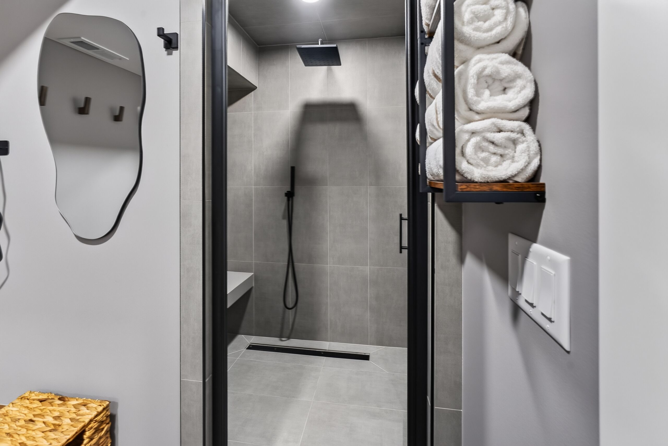 Un ba ño moderno con cabina de ducha de vidrio, un perchero con toallas enrolladas y un espejo con un marco curvo original.