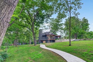 A modern house with a curved pathway leading to it, surrounded by lush greenery and trees.