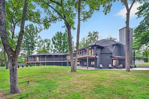 A modern two-story house with a flat roof, large windows, and a covered outdoor seating area.