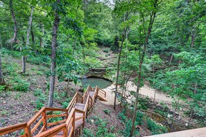 Eine Holzbrücke führt zu einem natürlichen Teich, umgeben von dichtem Wald.