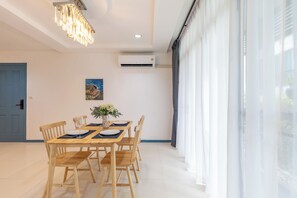 A dining area with a wooden table set for four, surrounded by chairs, a vase with flowers, and a painting on the wall. - The Regent Kamala Condominium by PSR (Tambon Kamala)