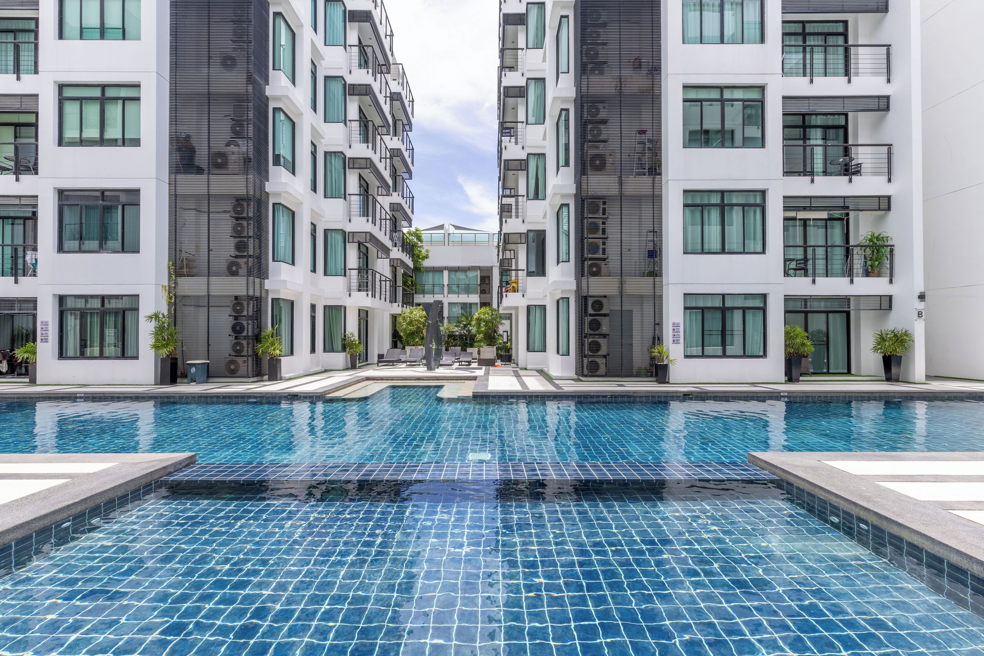Un immeuble résidentiel moderne doté d’une piscine centrale, de nombreux balcons et offrant une vue sur un ciel dégagé.