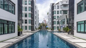 A modern building with a central swimming pool, surrounded by balconies and windows. - The Regent Kamala Condominium by PSR (Tambon Kamala)