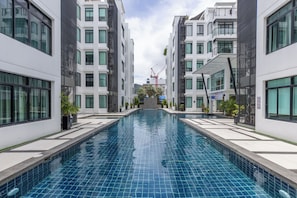 A modern building with a central swimming pool, surrounded by balconies and windows. - The Regent Kamala Condominium by PSR (Tambon Kamala)