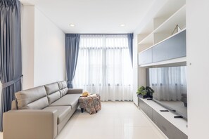 A modern living room with a sofa, a small table with a hat and book, and a TV on a stand. - The Regent Kamala Condominium by PSR (Tambon Kamala)