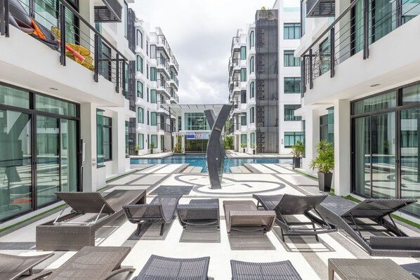A modern hotel atrium with a central pool, lounge chairs, and a geometric floor pattern. - The Regent Kamala Condominium by PSR (Tambon Kamala)
