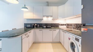 A modern kitchen with white cabinets, a built-in oven, a washing machine, and a coffee maker. - The Regent Kamala Condominium by PSR (Tambon Kamala)