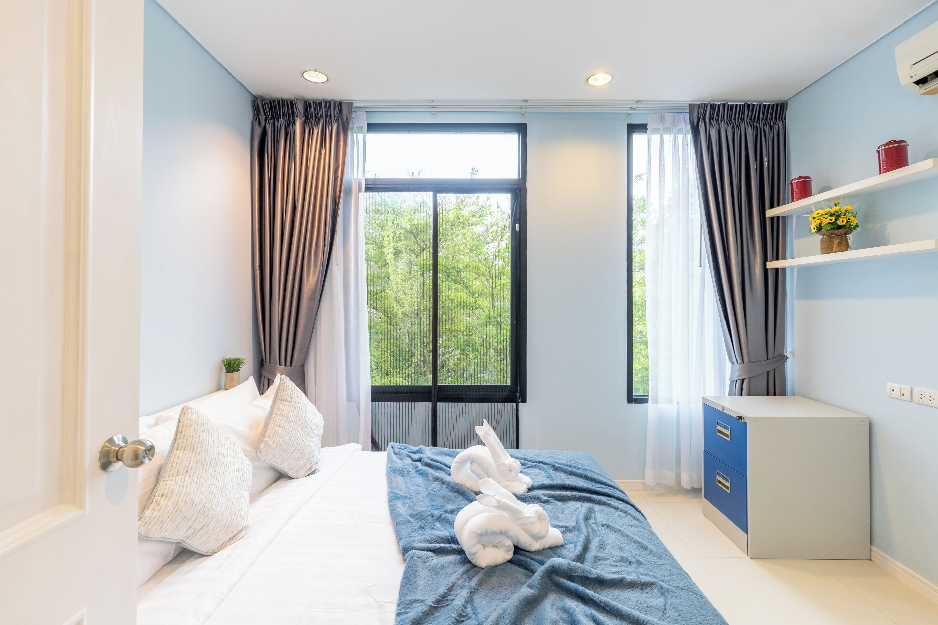 A modern bedroom with a bed, a blue blanket, a white sculpture, and a small cabinet.
