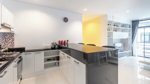 A modern kitchen with a central island, white cabinetry, and a black countertop. - The Regent Kamala Condominium by PSR (Tambon Kamala)