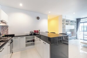 A modern kitchen with a central island, white cabinetry, and a black countertop. - The Regent Kamala Condominium by PSR (Tambon Kamala)