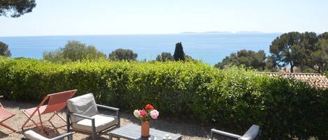 Un espacio al aire libre con sillas y una mesa, con vistas a una masa de agua y una costa lejana.