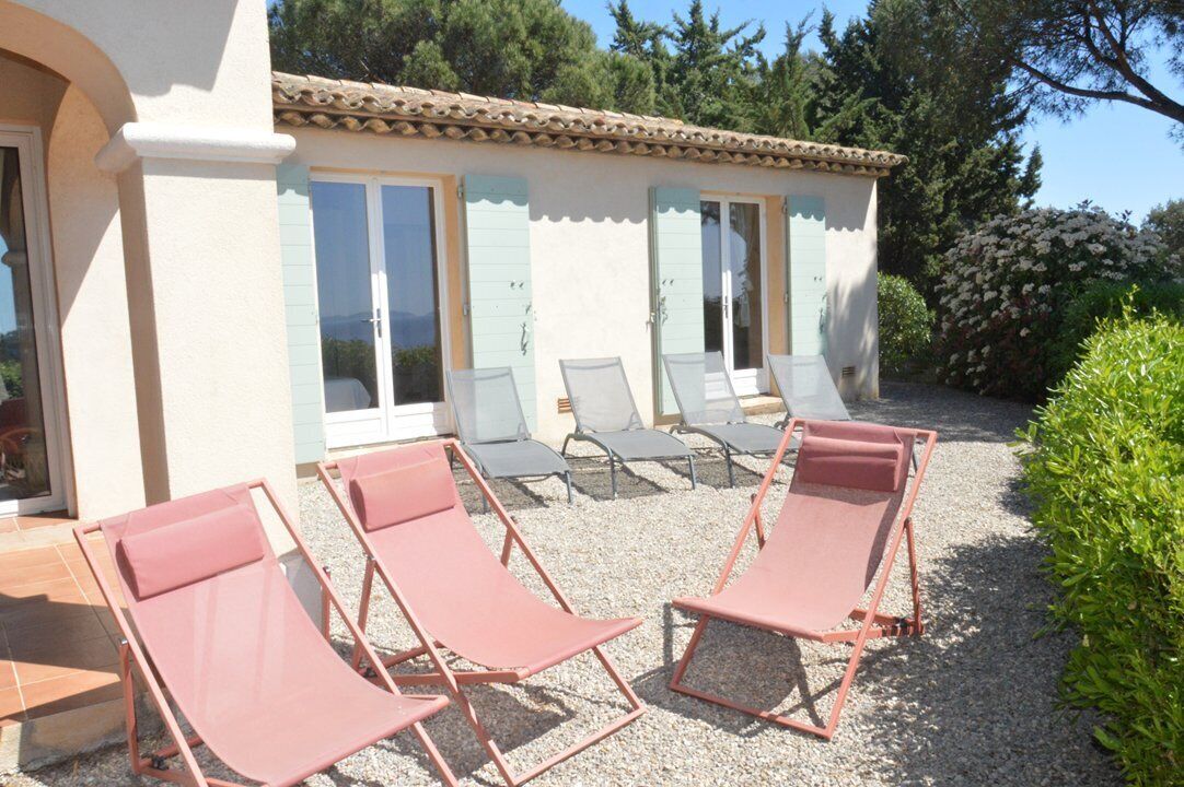 A building with a tiled roof, a covered patio with sun loungers, and a gravel ground.