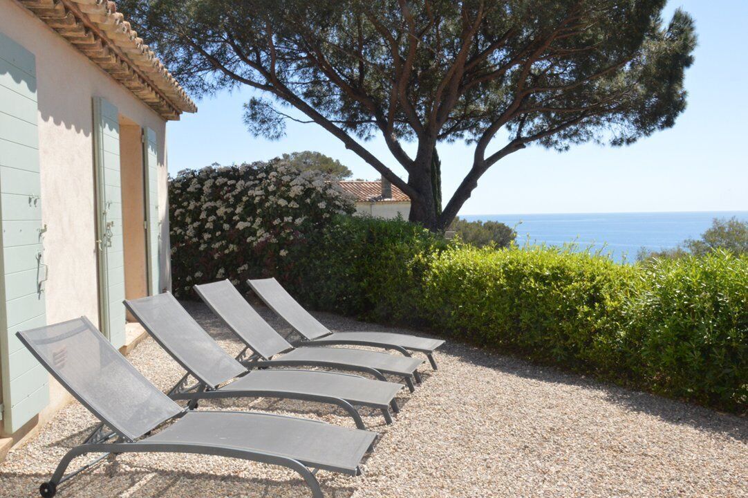 A row of sun loungers outside a building with a view of the sea.