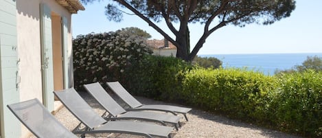 A row of sun loungers outside a building with a view of the sea.