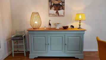 A light blue wooden cabinet with a glass top, a wicker lamp, a small giraffe figurine, a bowl of fruit, and a lamp with a yellow shade.