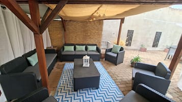 Un espace extérieur aménagé avec des meubles en osier, un tapis à motifs et une structure de pergola en bois.
