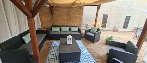 Ein Außenbereich mit Korbmöbeln, einem gemusterten Teppich und einer Holzwicker-Pergola.