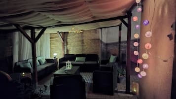 Un espace extérieur aménagé avec des sièges, une partie abritée, des meubles en osier et des éclairages décoratifs.