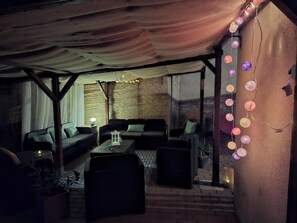 Een terras met overdeeld gedeelte, rieten meubels en decoratieve verlichting.