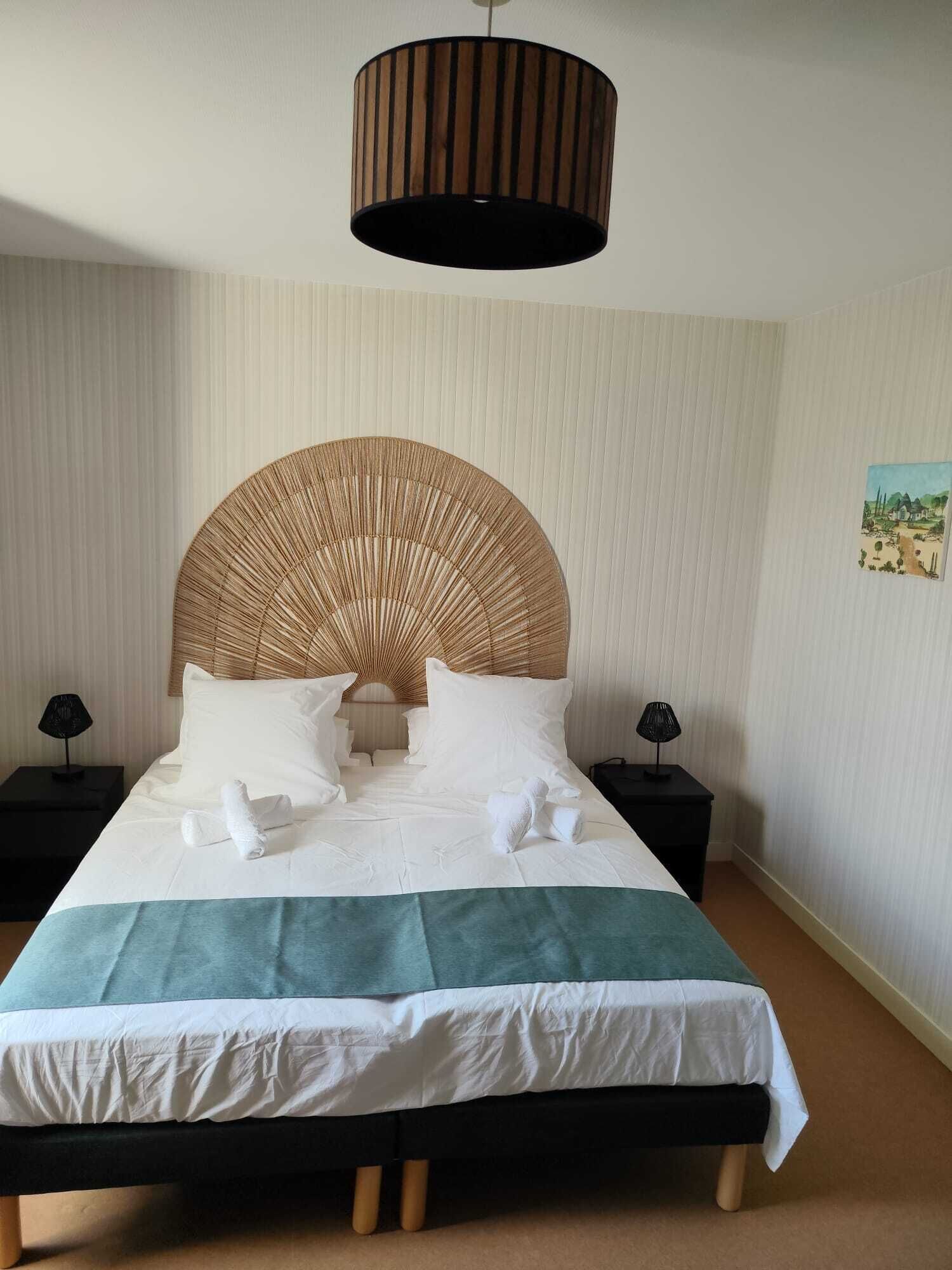 A neatly made bed with white linens and a green throw blanket, a large woven headboard, and two bedside tables with lamps.
