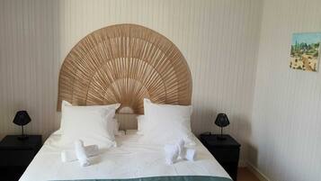 A neatly made bed with white linens and a green throw blanket, a large woven headboard, and two bedside tables with lamps.