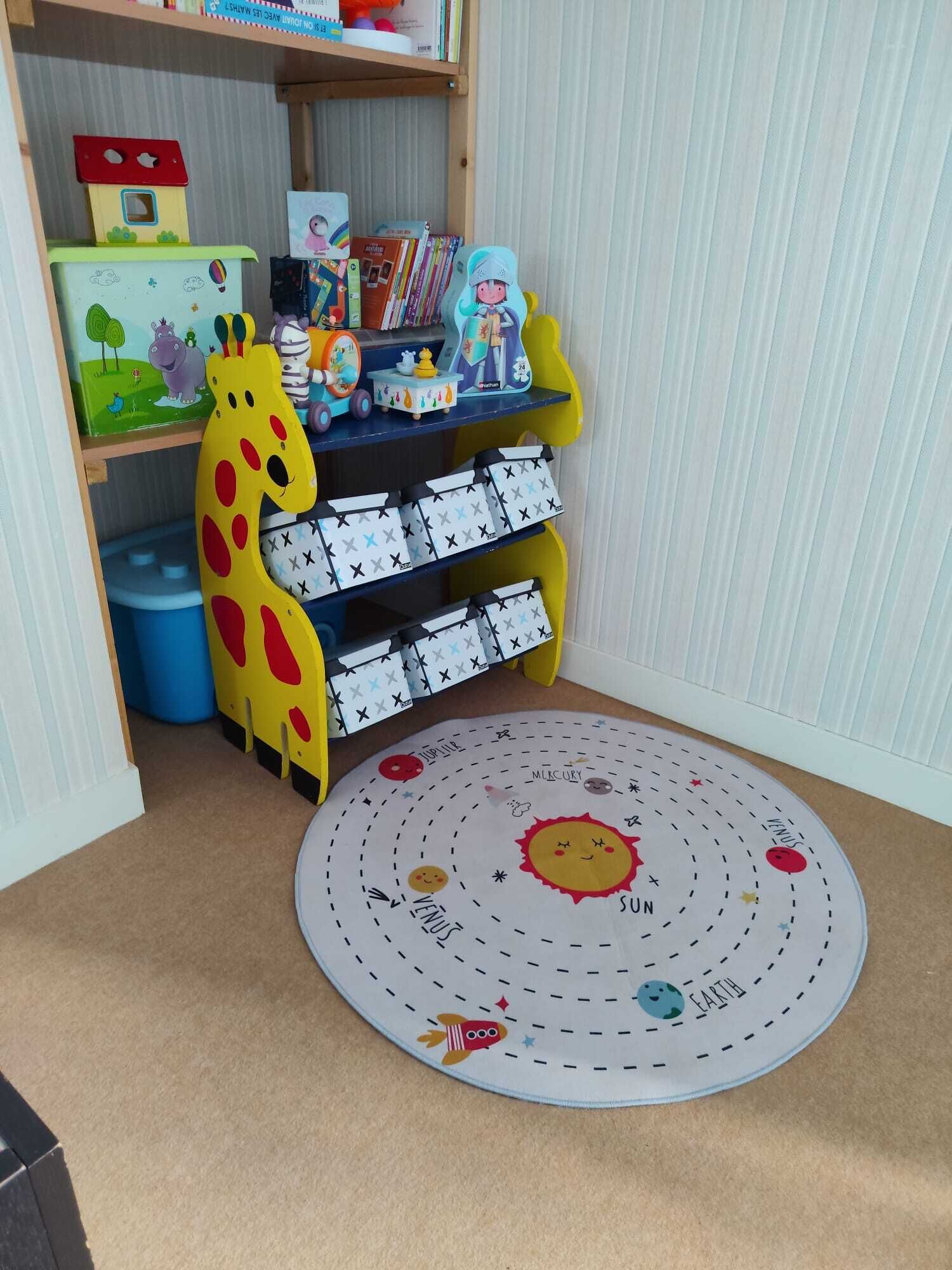 Ein Kinderspielbereich mit Bücherregal, Giraffenspielzeug und einer Matte mit dem Sonnensystem.