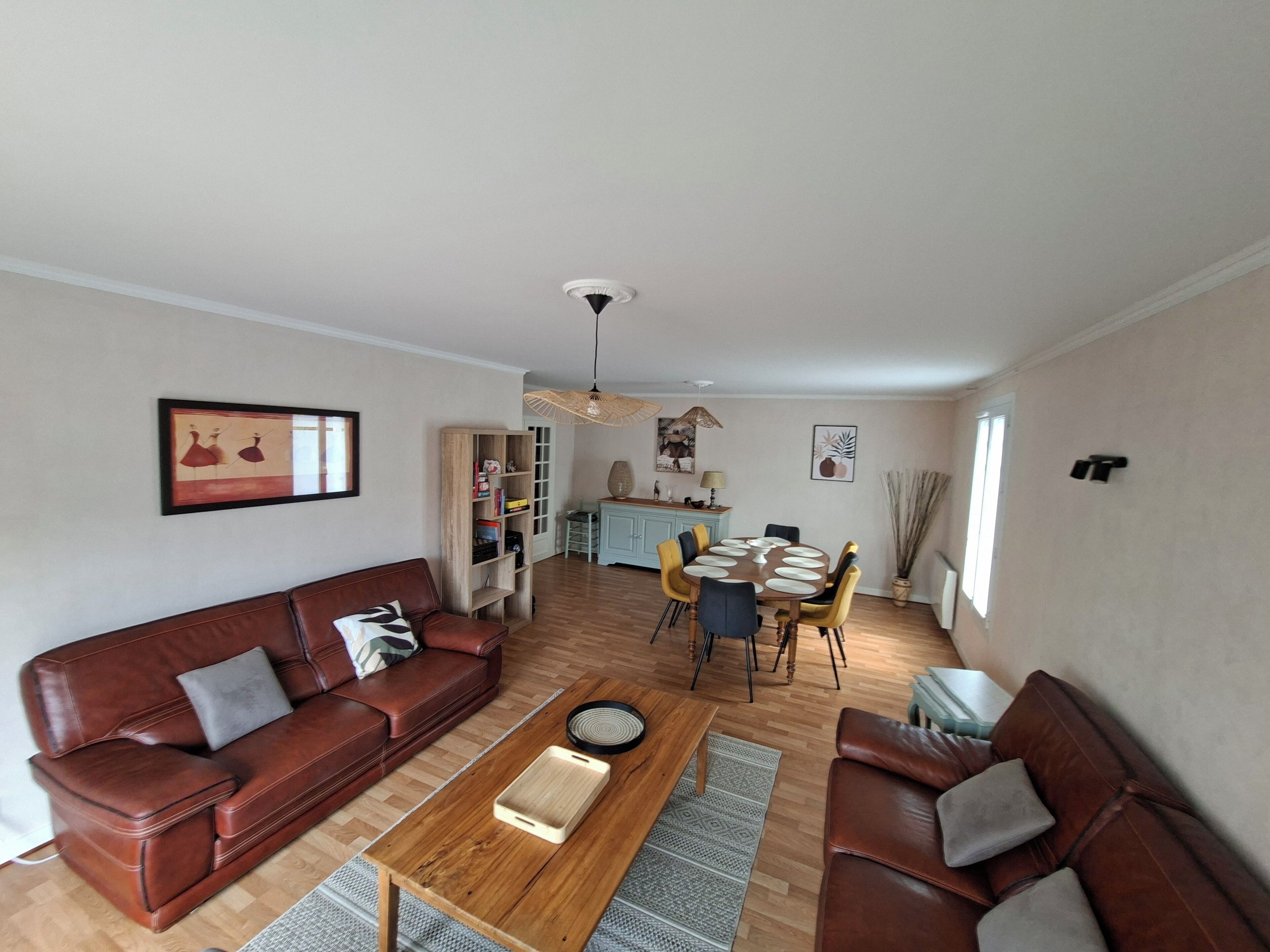 Un salon avec un canapé en cuir marron, une table basse en bois et un coin repas comprenant une table ronde et des chaises.