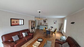 Un salon avec un canapé en cuir marron, une table basse en bois et un coin repas comprenant une table ronde et des chaises.