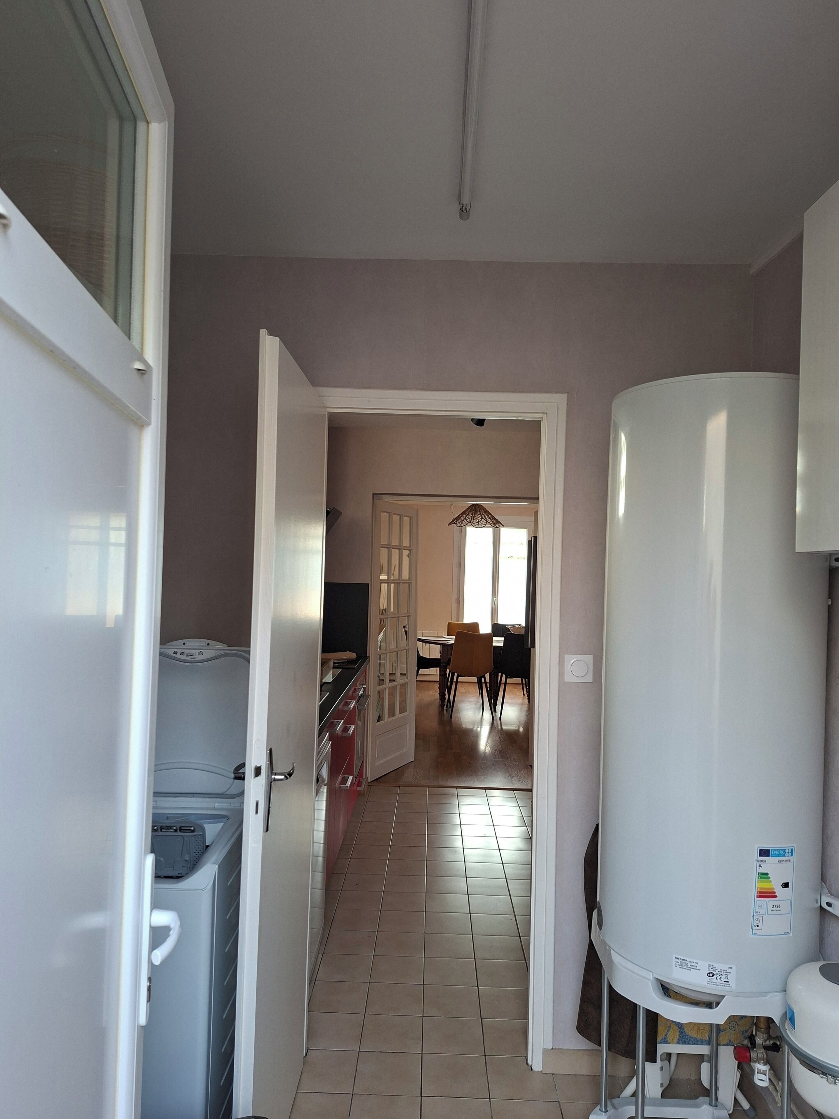 Ein Flur mit Warmwasserbereiter, ein Essbereich mit Stühlen und Tisch sowie eine Küchenzeile mit Schränken.