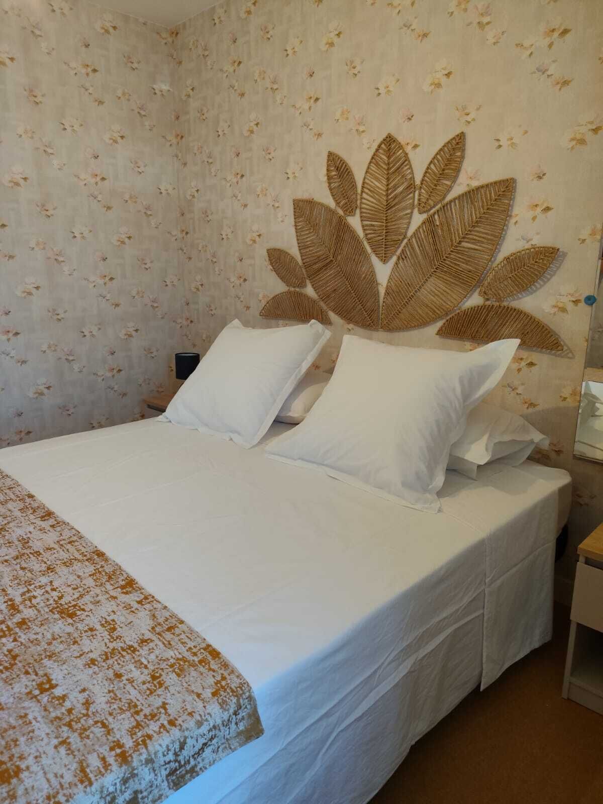 A bed with white bedding and a large woven leaf headboard.